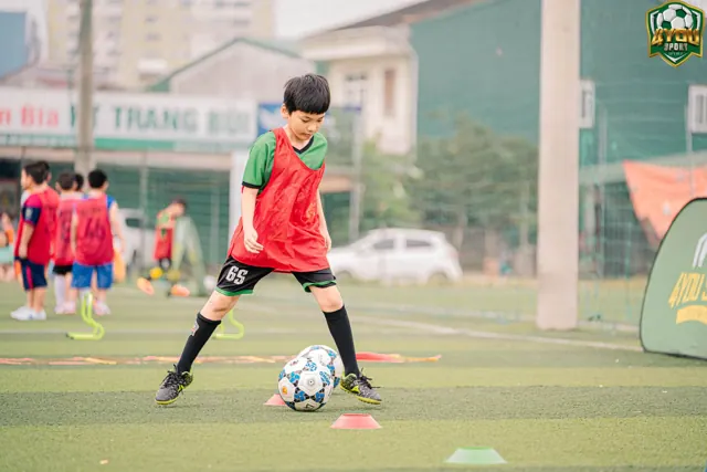 Bé sút bóng trong bài tập kỹ thuật, có cọc đĩa trên sân